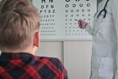 Ophthalmologist holds pen to check vision of teenage boy child. Eye test chart and vision test for adults and children
